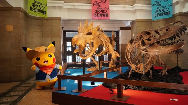 Excavator Pikachu mascot next to Tyrannosaurus and Tyrantrum skeletons at the Pokemon Fossil Museum