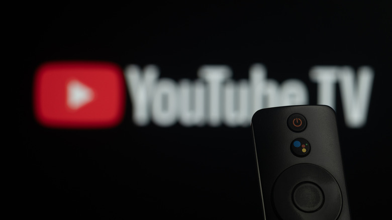 Close-up of a smart TV remote control against a blurred Youtube TV logo.