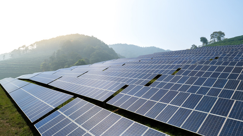 A field covered in solar panels with grassy mountains behind it