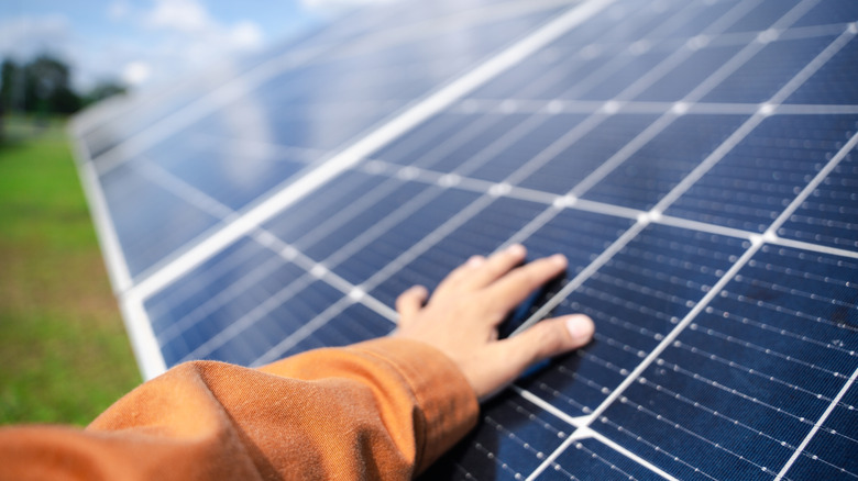 A hand touches a black monocrystalline solar panel