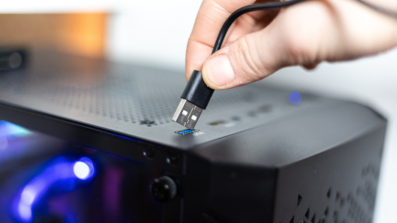 person plugging a usb cable into a blue usb port on top of a computer case