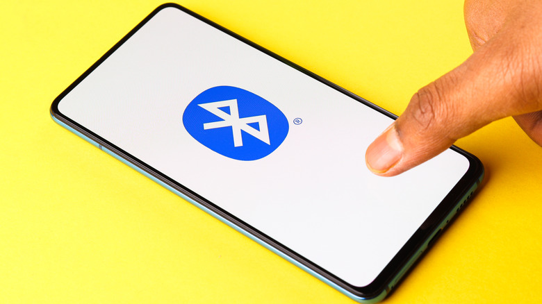 A phone lying on a bright yellow table displaying the Bluetooth icon on its screen