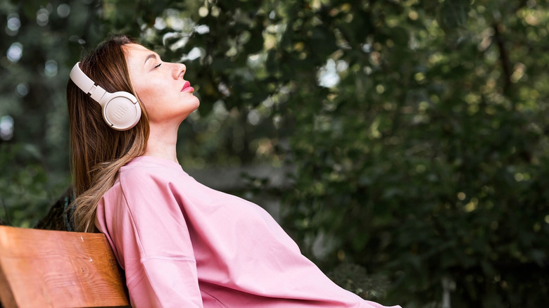 A woman relaxing on a bench listening to wireless headphones.
