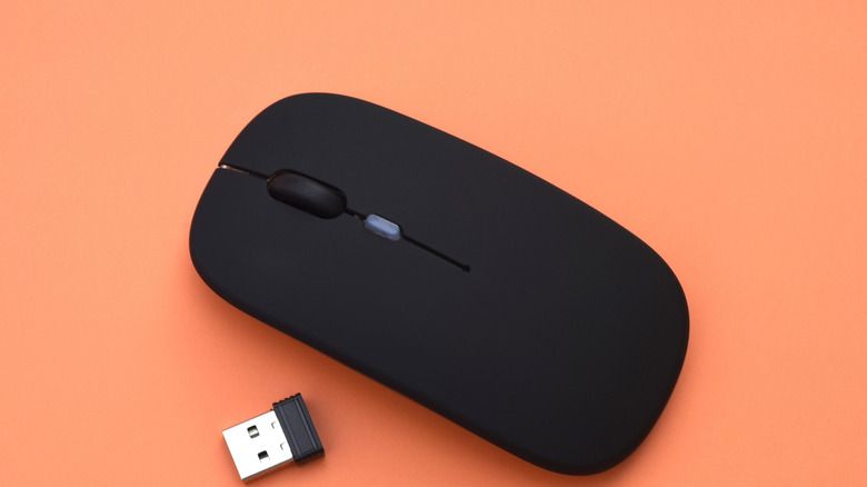 A wireless mouse with its USB dongle against an orange backdrop