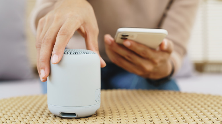 A person holding a phone next to a portable Bluetooth speaker.