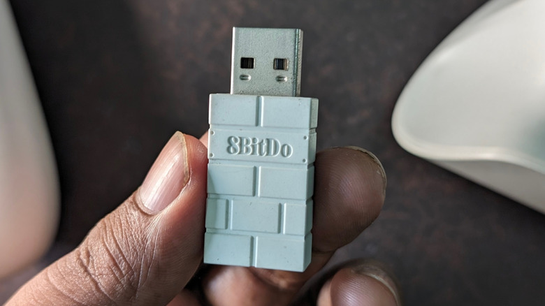A person holding a USB-RF dongle for a wireless game controller.