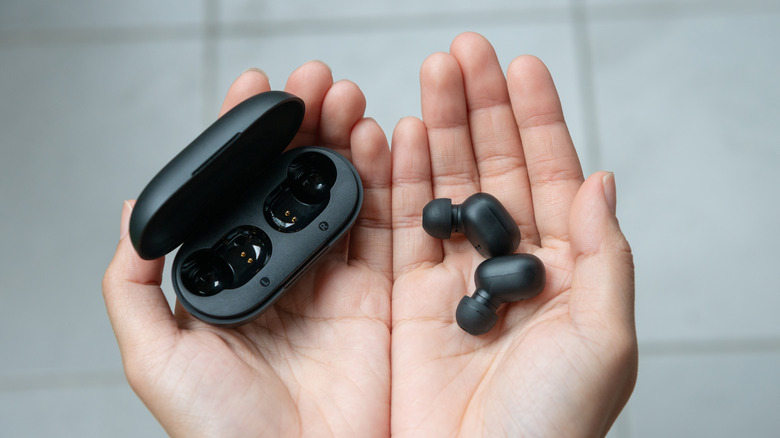 Hands holding a pair of wireless earbuds and their empty battery case