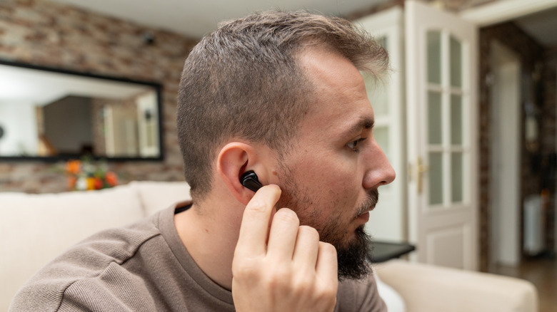 A man sitting on a couch with a Bluetooth earbud in his ear