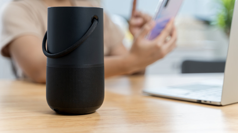 A Bose speaker sitting on a table near a laptop