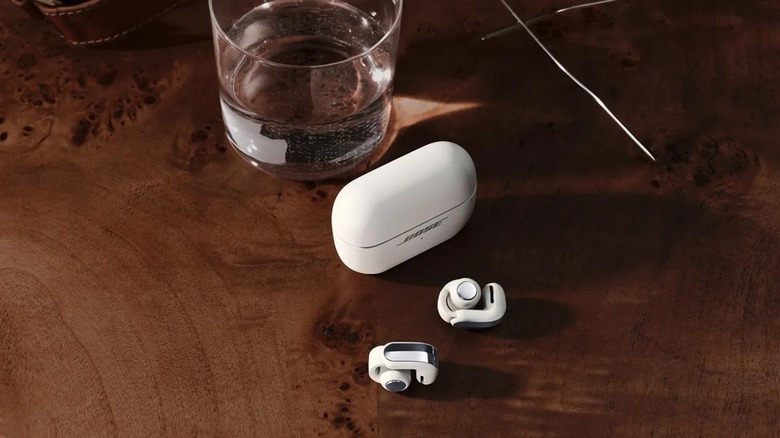 Bose Ultra Open Earbuds 2nd Gen in white on a wooden table next to a glass of water