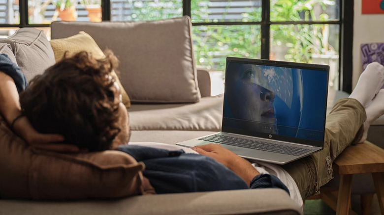 A man reclining in a couch with the HP OmniBook 5 16-inch laptop on his lap.