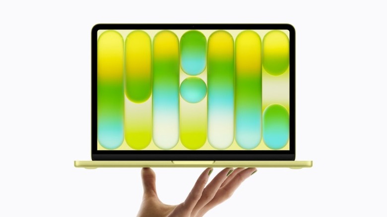 A person's hand holding up a yellow Apple MacBook Neo laptop.