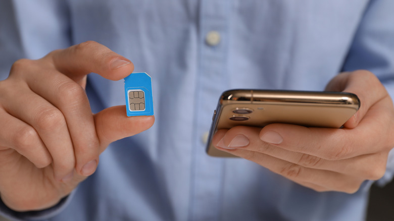 Someone holding a phone in one hand and a SIM card in the other.