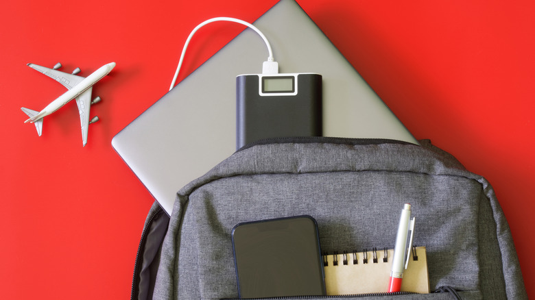 Power bank charging a laptop beside travel essentials and a backpack.