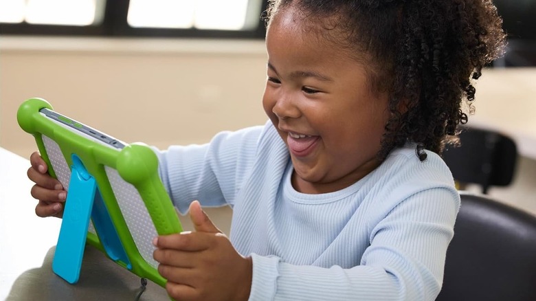 A little girl smiles as she plays with the LeapFrog LeapPad Academy Kids Learning Tablet