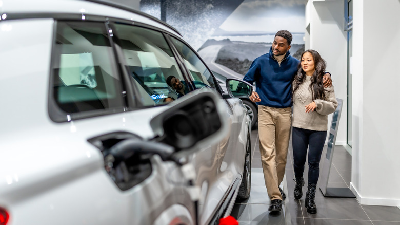Couple reviewing an electric vehicle which is plugged in and charging.