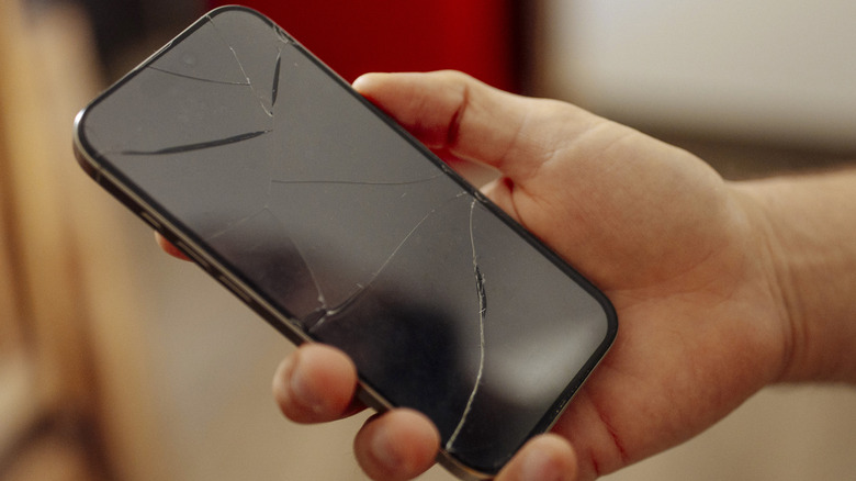Man holding a phone with a cracked screen