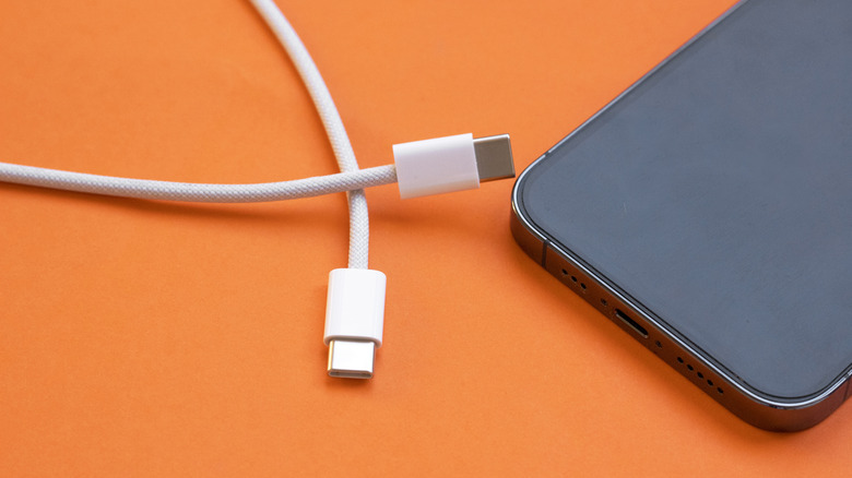 A USB-C to USB-C charger next to a smartphone on an orange background