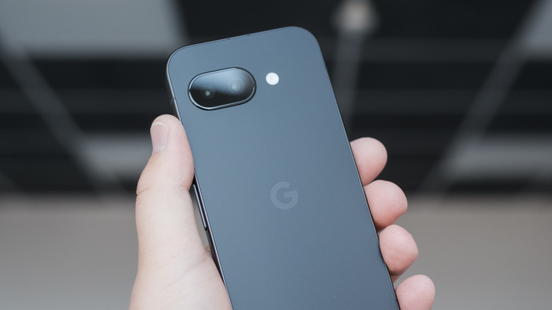 A user holds a black Google Pixel 9A in their hand, the background too blurred to be made out fully