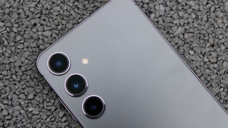 A silver Galaxy S24 sits across a background composed of small, grey pebbles