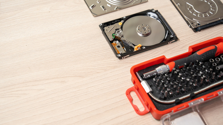 An unassembled hard drive being repaired on a table with a tool box on the side