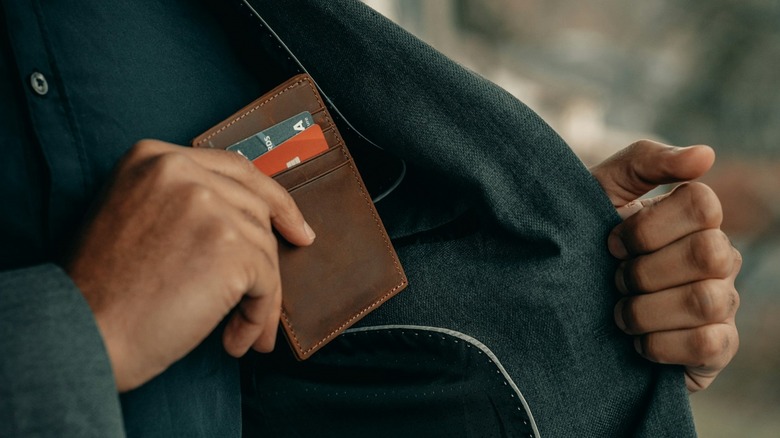 Man sliding RFID wallet with credit cards visible into jacket pocket.