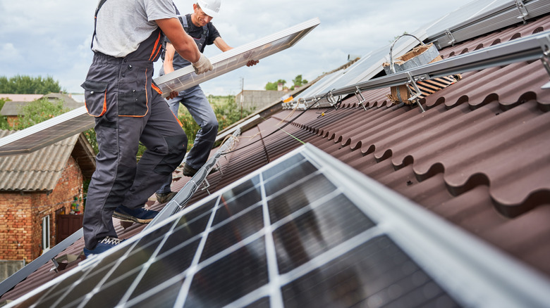 Technicians replace a solar panel on a residential roof