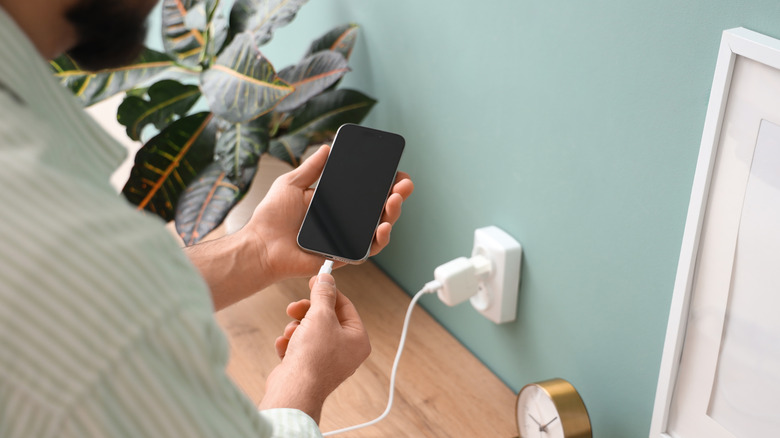 Close-up of a man plugging a smartphone into a wall charger.