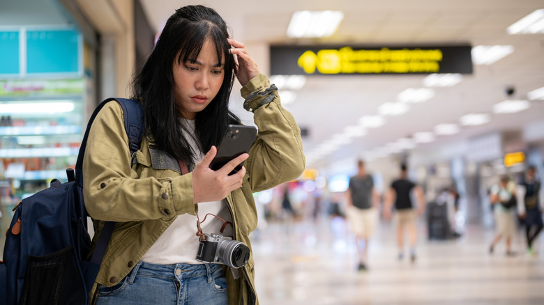 a woman looking at her phone confused in an airport