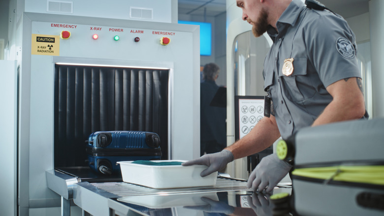 A TSA employee guiding objects into a CT scanner.