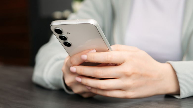 A pair of hands with pink nail polish holding a white Samsung smartphone
