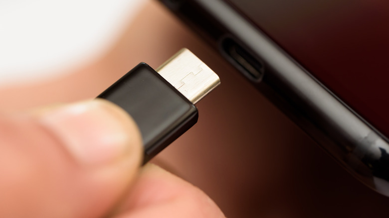 Person inserting black USB-C cable into black smartphone port