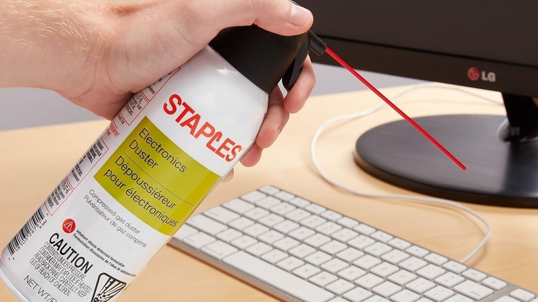 Person holding staples compressed air cannister to clean keyboard