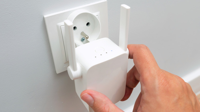 A person plugging Wi-Fi range extender into an open European-style outlet.