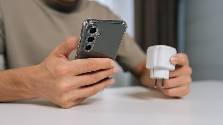Person holding a white smart plug in one hand and a smartphone in another