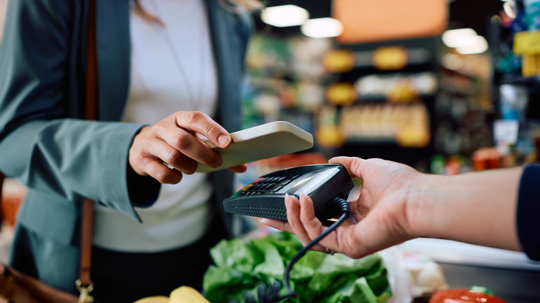 Close-up of a person tapping a phone to pay for groceries