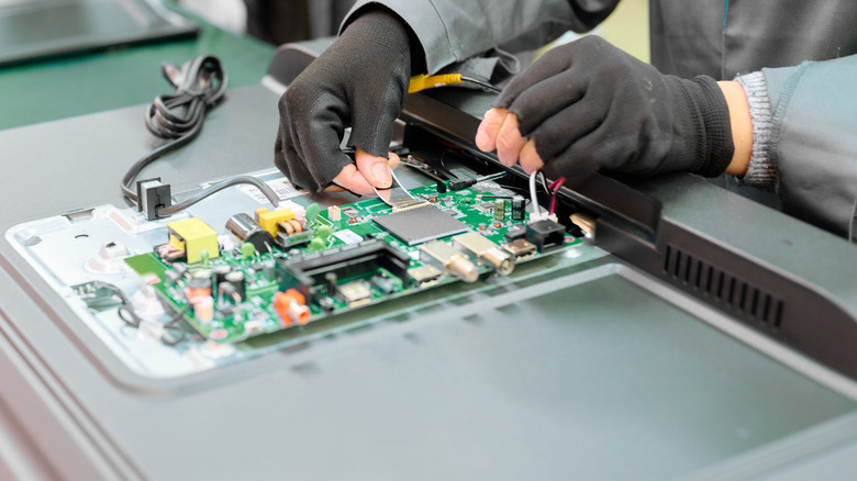 A worker assembling electronic components on a TV circuit board panel