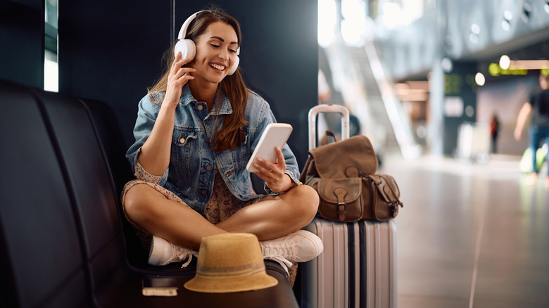 Woman listening to wireless headphones connected to her phone, in an airport.