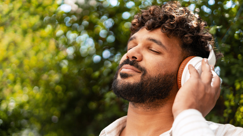 Man listening to wireless headphones outdoors with greenery behind him.