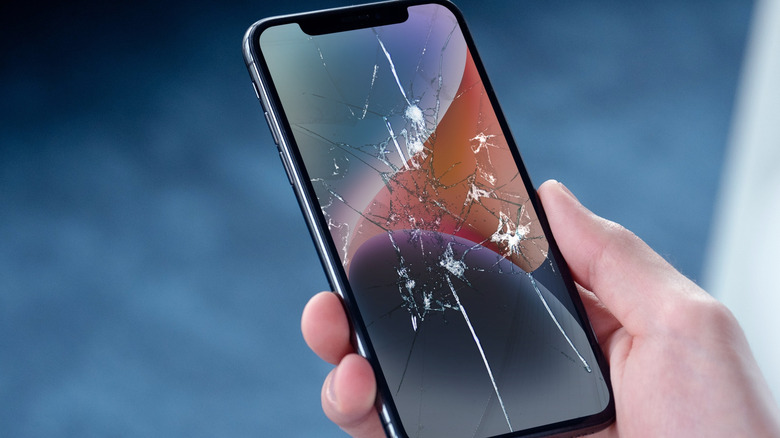 A person using an iPhone with a badly cracked screen.