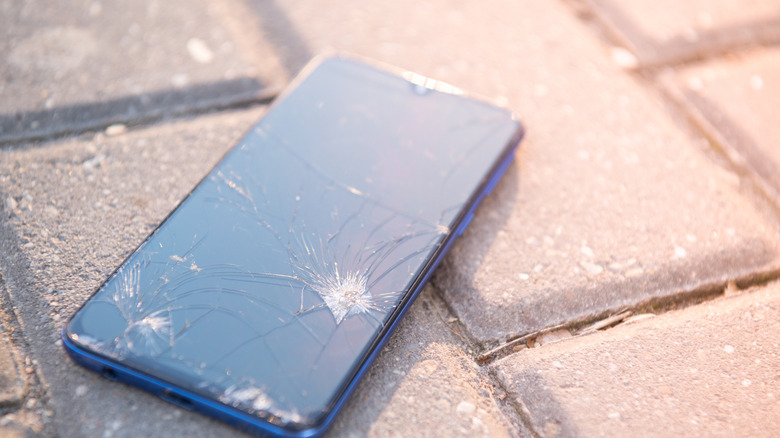 A smartphone with a cracked screen on the ground.