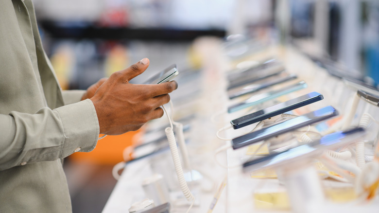Person browsing smartphones on display in an electronics store.