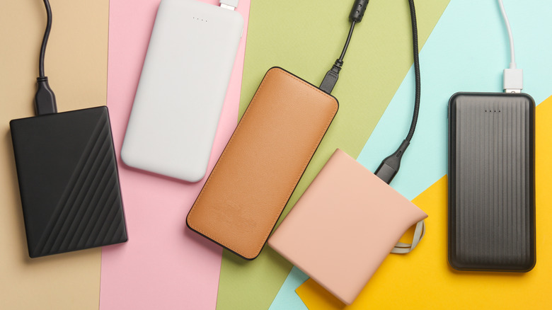 Five portable battery packs of various colors, each one loosely set against its own solid color.
