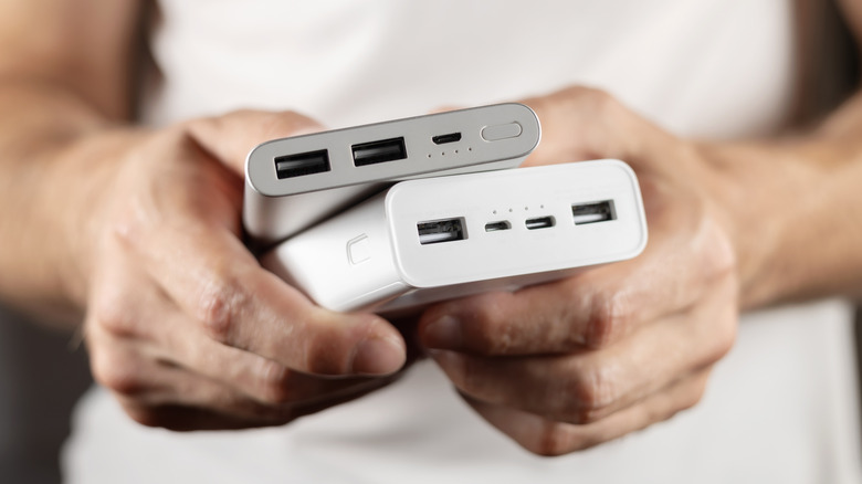 A person holding two portable batteries, one silver and one white, on top of each other.