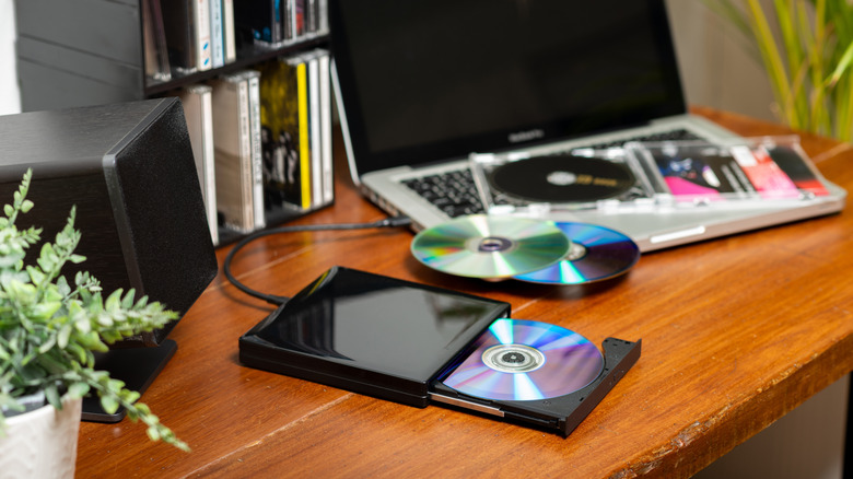 A pile of discs including DVDs and CDs with a disc drive.