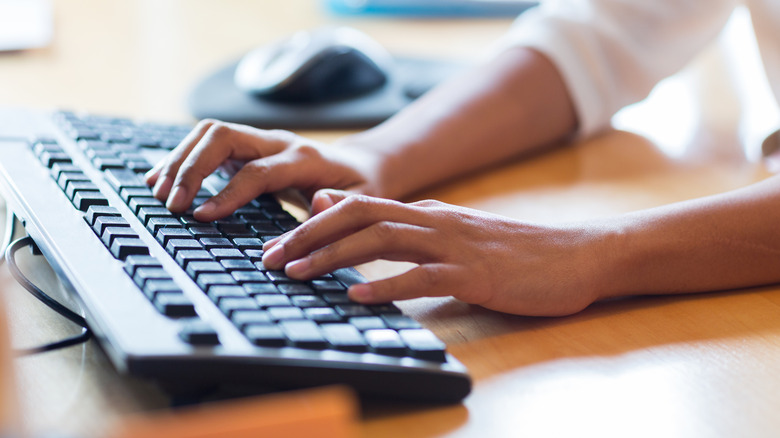 Hands typing on a computer keyboard with mouse in background