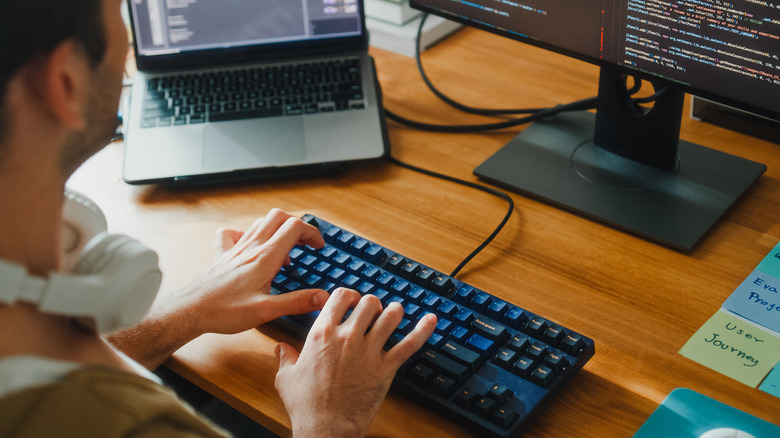 Person coding on desktop computer while typing on mechanical keyboard