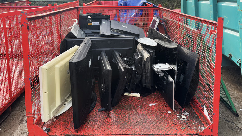 Several TVs, monitors, and displays on a recycling bin