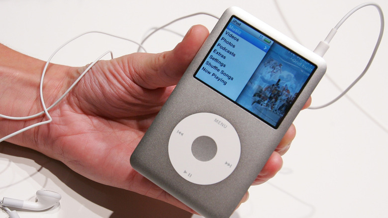 Someone holding an iPod Classic media player (6th generation) with wired headphones.