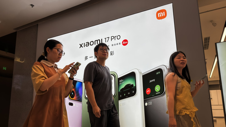 Shoppers walk past an advertisement for the Xiaomi 17 Pro Android smartphone.